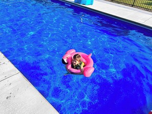 Un enfant, dans un flotteur de piscine gonflable rose, se trouve dans une piscine à l’eau d’un bleu limpide.