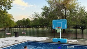 A swimming pool with a basketball hoop, surrounded by a fence and trees. - Airstream w flush toilet, city water, hot tub (Comanche County)