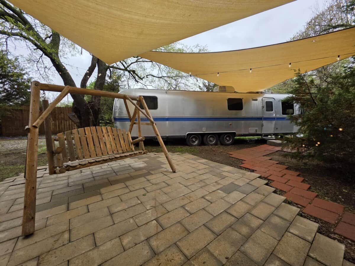 A patio area with a swing set and a camper parked in the background.