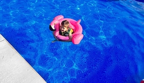 A child in a pink inflatable pool float in a swimming pool.