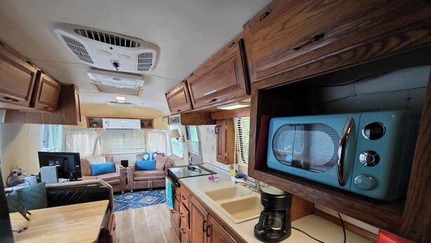 A compact RV kitchen with a microwave, coffee maker, and wooden cabinets. - Airstream w flush toilet, city water, hot tub (Comanche County)
