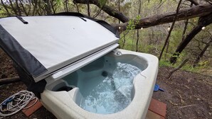 A hot tub with a white exterior, surrounded by a natural forest setting. - Airstream w flush toilet, city water, hot tub (Comanche County)
