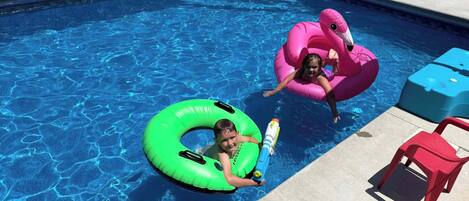 A swimming pool with inflatable rings and lounge chairs.