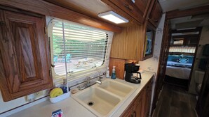 A compact RV kitchen with a sink, a coffee maker, and a window with blinds. - Airstream w flush toilet, city water, hot tub (Comanche County)