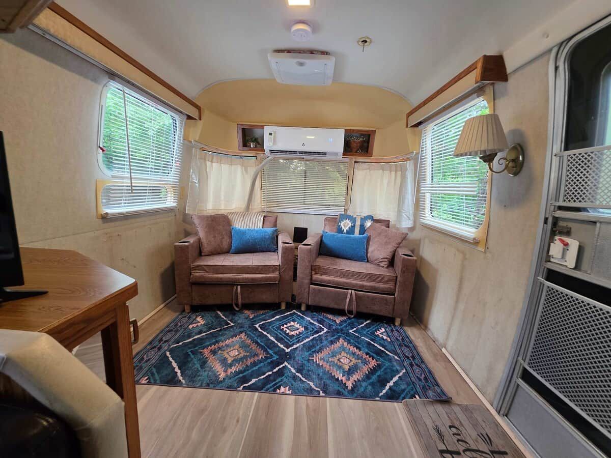 A compact RV interior with two sofas, a small table, and a patterned rug.