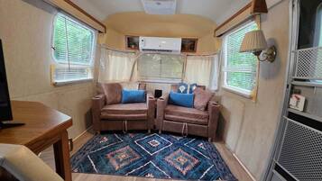 A compact RV interior with two sofas, a small table, and a patterned rug.