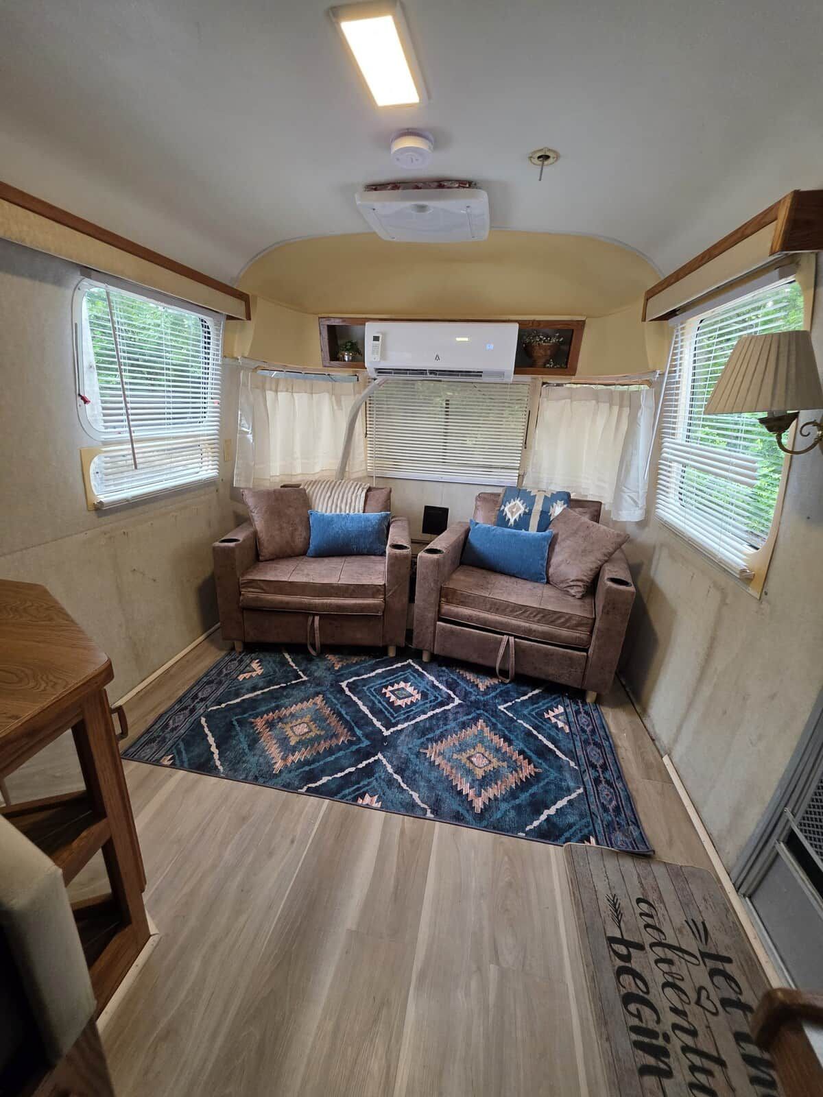 Een ruimtelijk ingericht camperinterieur met twee banken, een kleine tafel en een vloerkleed met dessin.