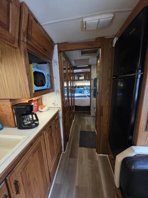Ein kompaktes Wohnmobil-Interieur mit Holzschränken, einer Küchenzeile, einem Bett und einem Kühlschrank.