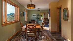 A dining area with a wooden table and chairs, large windows with a view, and a patterned rug.