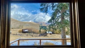 A window view of a rural landscape with a wooden fence, a barn, and a tree.