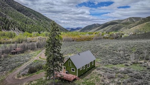 A green house with a deck, surrounded by a mountainous landscape and a clear sky.