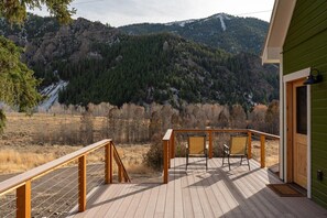 A wooden deck with two chairs and a view of a forested mountain. - Triumph Ranch Farm House (Hailey)