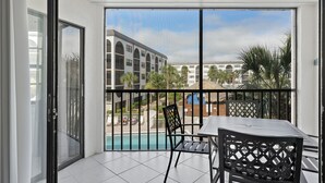 A balcony with a table and chairs, overlooking a swimming pool and a building with arched windows. - NEW LISTING!  Adorable condo, everything is new! Fantastic location! (Marco Island)