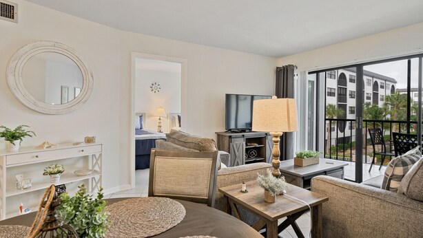 A modern living room with a sofa, armchair, and coffee table. There is a television, a lamp, and a large window with a view of buildings. - NEW LISTING!  Adorable condo, everything is new! Fantastic location! (Marco Island)