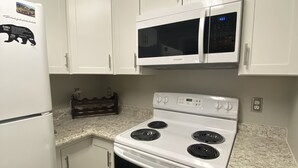 A kitchen with white cabinets, a white refrigerator, a microwave, and a stove.