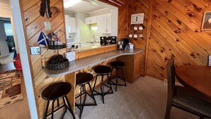 A cozy kitchen with wooden walls, a bar area with stools, and a coffee station.