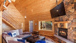 A log cabin interior with a stone fireplace, wooden ceiling, and a sofa with cushions. - Log Cabin near Historic Cripple Creek, Hot Tub and Spectacular Views! (Cripple Creek)