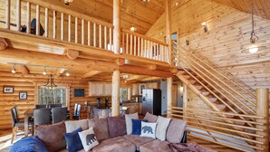 A log cabin interior with a wooden staircase, a dining area, and a living room with a sectional sofa. - Log Cabin near Historic Cripple Creek, Hot Tub and Spectacular Views! (Cripple Creek)