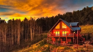 A wooden cabin with a balcony, surrounded by a forest and a rocky terrain. - Log Cabin near Historic Cripple Creek, Hot Tub and Spectacular Views! (Cripple Creek)