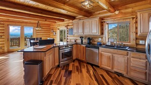 A log cabin kitchen with wooden cabinets, a stainless steel refrigerator, and a large island with a sink and stove. - Log Cabin near Historic Cripple Creek, Hot Tub and Spectacular Views! (Cripple Creek)