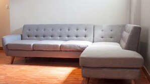 Ein graues Ecksofa mit gepolsterten Sitzfläche und Rückenlehne, stehend auf einem Holzboden.
