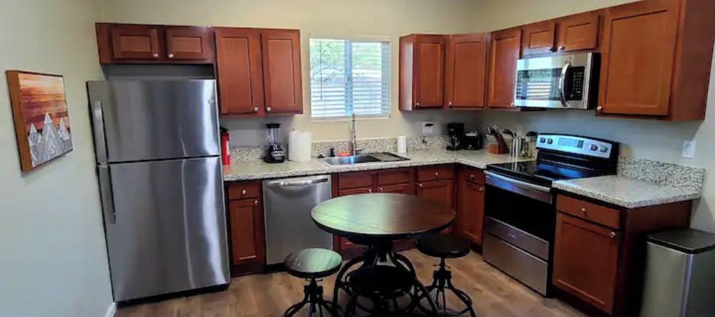 A kitchen with wooden cabinets, stainless steel appliances, a granite countertop, and a dining table with stools.