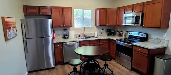 A kitchen with wooden cabinets, stainless steel appliances, a granite countertop, and a dining table with stools.