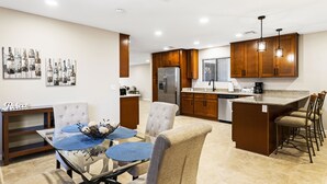 A modern kitchen with a central island, bar stools, and a dining area with a glass table and chairs.