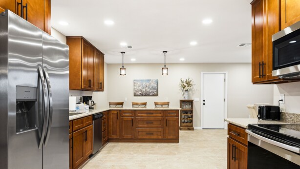 A modern kitchen with wooden cabinets, stainless steel appliances, and a tiled floor.