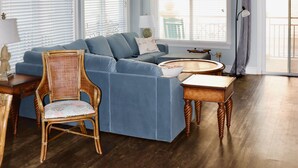 A spacious living room with a blue sofa, a wooden chair, a coffee table, and a ceiling fan. - Oceanfront Penthouse Overlooking the Atlantic Ocean (Daufuskie Island)
