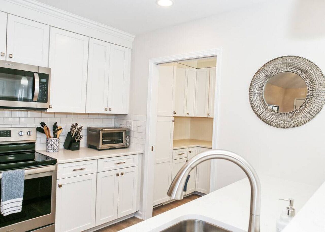 A kitchen with white cabinets, a microwave, a toaster, and a sink with a modern faucet.