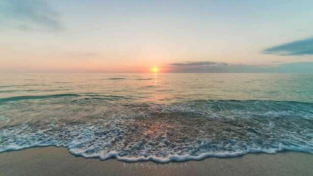 A beach with waves and a sunset in the distance.