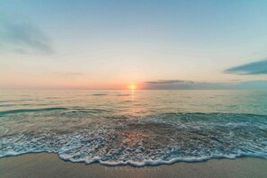 A beach with waves and a sunset in the distance.