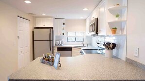 A modern kitchen with white cabinets, a granite countertop, a refrigerator, a microwave, and a sink.