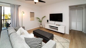A modern living room with a sofa, a coffee table, a TV on a white stand, a ceiling fan, and a sliding door closet.