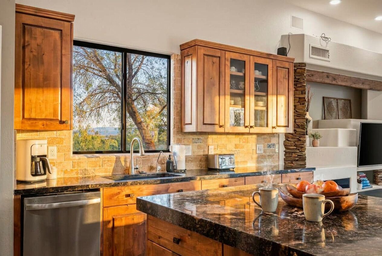 A kitchen with wooden cabinets, a stone accent wall, a large window, and a countertop with a coffee maker and mug.