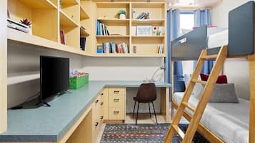 A compact room with a bunk bed, a desk with a computer, a chair, and built-in shelves with books and decorative items.