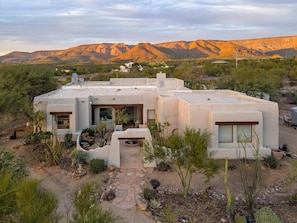 A modern house with a flat roof, surrounded by desert vegetation and mountains in the background. - 6 Hole Golf | Hot Tub | Pool+More | Featured on TV show Staycation (Phoenix)