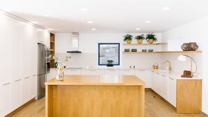 A modern kitchen with white cabinets, a wooden island, stainless steel appliances, and decorative plants. - Casa Vieira Lobo (Arouca)
