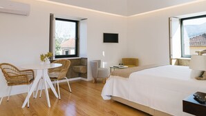 A modern hotel room with a large bed, a seating area with chairs, a flat-screen TV, and large windows offering a view of the outdoors. - Casa Vieira Lobo (Arouca)