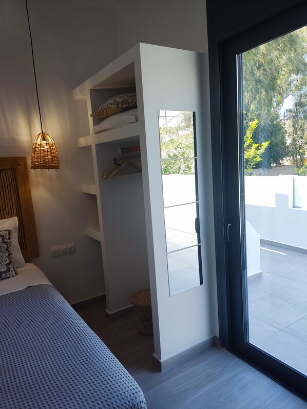 A bedroom with a bed, a hanging light, a wardrobe, and a sliding glass door leading to an outdoor area. - Callas Residence (Rhodes)