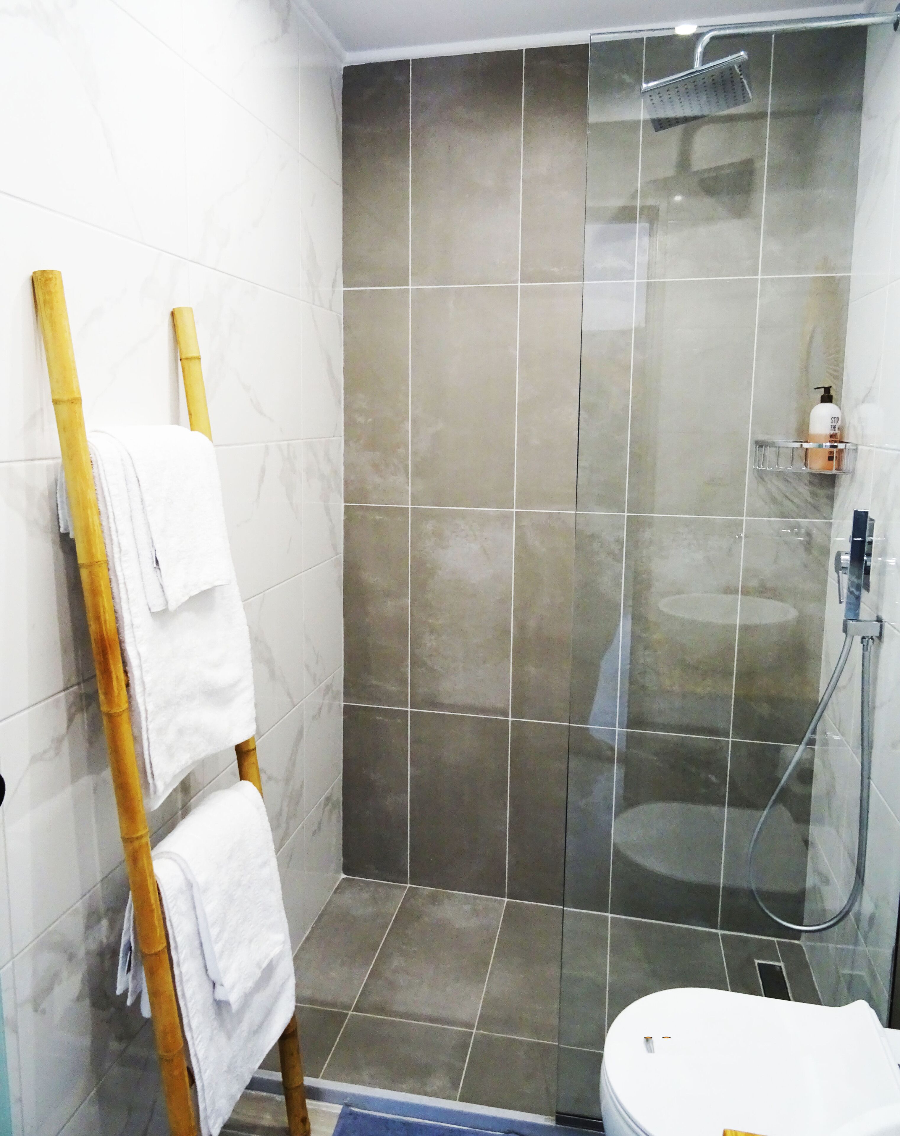 A bathroom with a shower, toilet, and a bamboo towel rack.