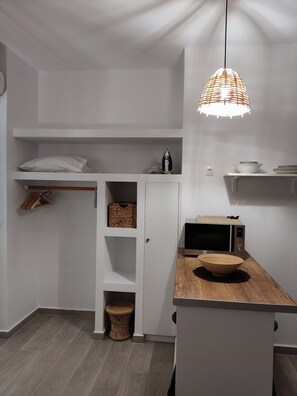 A modern kitchen with white cabinetry, a wooden countertop, a hanging light fixture, and a microwave.