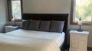 Ein Schlafzimmer mit Bett, Deckenventilator, Nachttischen und Fenstern.