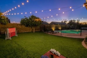 A backyard with artificial string lights, a pool, and a fenced area.
