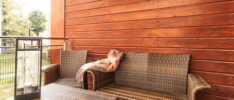 A wicker sofa with a cushion and a throw blanket against a wooden wall.