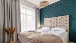 A neatly made bed with a tufted headboard, a vase with dried plants, and a window with sheer curtains. - Sopot Marina (Sopot)