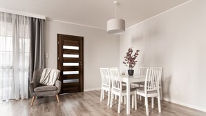 A dining area with a wooden floor, white chairs, a table with a potted plant, and a grey armchair. - Sopot Marina (Sopot)