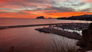 En kysthavn med fortøjede både, en klippefyldt bølgebryder og en solnedgang over vandet.