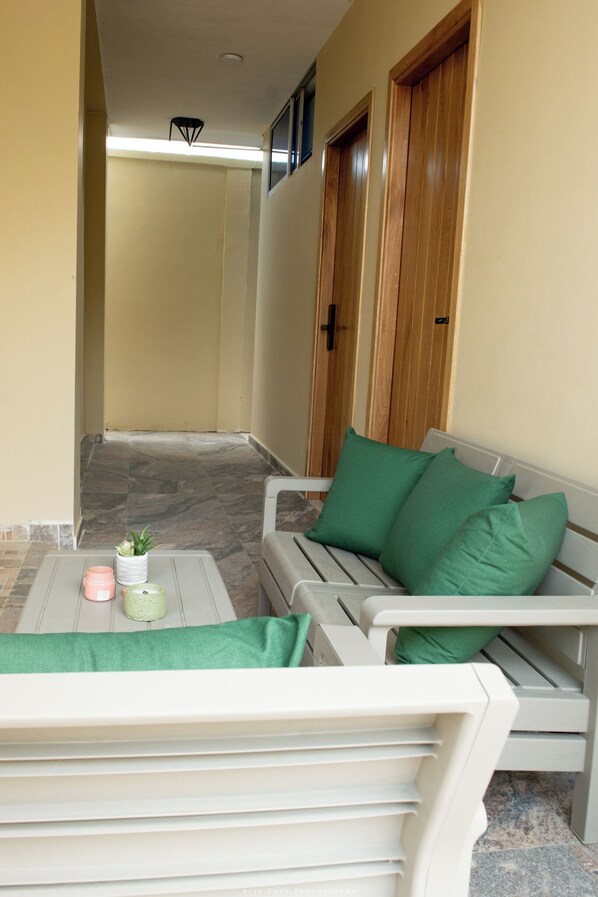 Un pasillo con un sofá blanco y cojines verdes, una mesita con una planta y una vela, y puertas de madera.